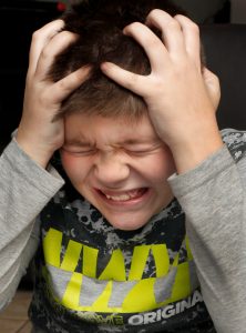 Young boy pulling a frustraded face with his hands on his head. He looks stressed and upset